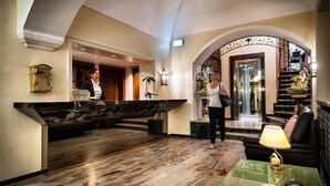 A lobby with a marble reception desk, a staircase, and a seating area with a lamp. - Dell Angelo (Locarno)