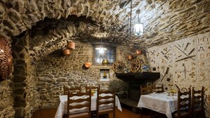 A rustic stone-walled dining area with wooden tables and chairs, a stone fireplace, and wall-mounted cutlery. - Dell Angelo (Locarno)