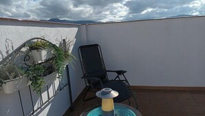 A rooftop terrace with a black chair, a small table with a glass top, and potted plants against a white wall. - San Francisco (Ronda)
