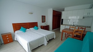 Ett hotellrum med en dubbelsäng, ett litet skrivbord, en stol, ett litet kök och en garderob.