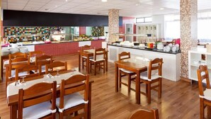 En restaurang med träbord och stolar, ett område med buffé och ett kök synligt längre in i lokalen.