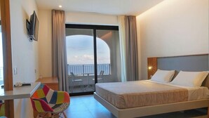 Une chambre d’hôtel avec un lit, un bureau, une chaise colorée et un balcon avec vue.