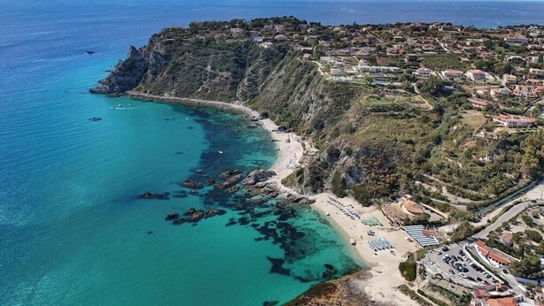 Vue aérienne d’une ville côtière avec une plage, une côte rocheuse et des immeubles résidentiels.
