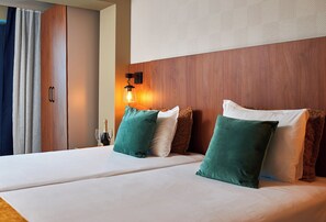 Quarto de hotel com uma cama grande, uma mesinha de cabeceira, uma garrafa de champanhe e um abajur fixado na parede.