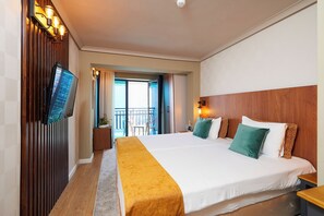 Habitación de hotel con una cama grande, un televisor montado en la pared, un balcón con vistas y un cabecero de madera.
