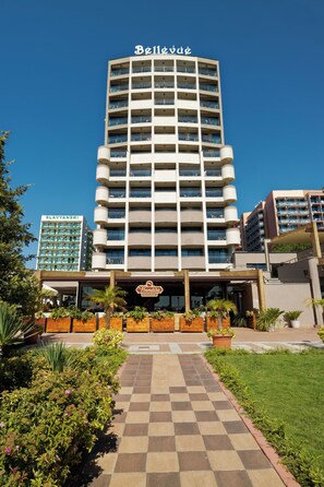 Un hotel de varios pisos con una entrada central, balcones en cada planta y un cielo despejado.