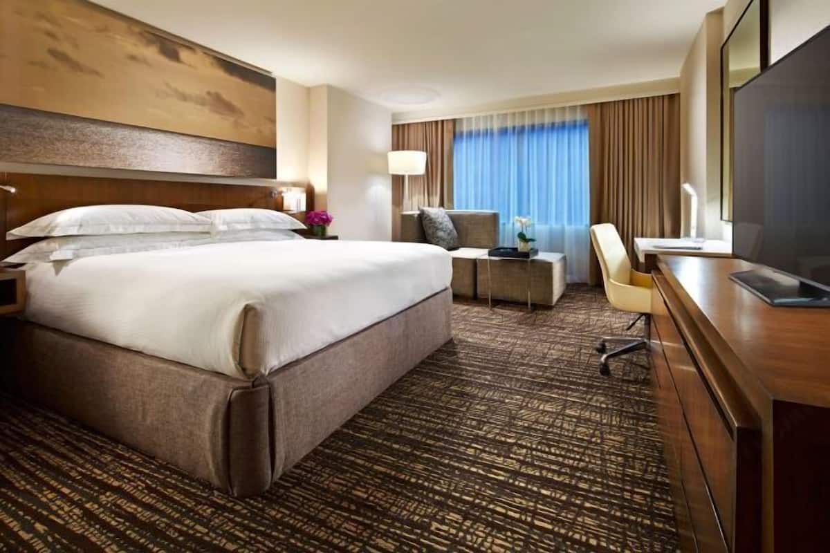 Une chambre d’hôtel avec un grand lit, un bureau avec une chaise, une télévision et une fenêtre avec des rideaux.