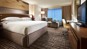Ein Hotelzimmer mit einem großen Bett, einem Schreibtisch mit Computer, einem Fernseher und einem Fenster mit Vorhängen.
