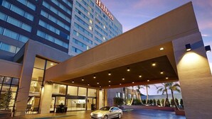 Une entrée d’hôtel moderne avec une allée couverte, une voiture garée devant et un bâtiment portant l’enseigne « Hilton ».