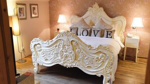 Een slaapkamer met een decoratief bed, twee nachtkastjes en een wand met bloemenbehang.