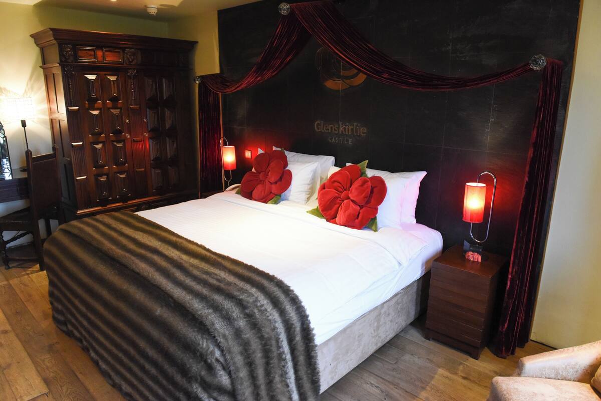 Une chambre d’hôtel avec un grand lit, une armoire en bois sombre et une table de chevet avec une lampe.