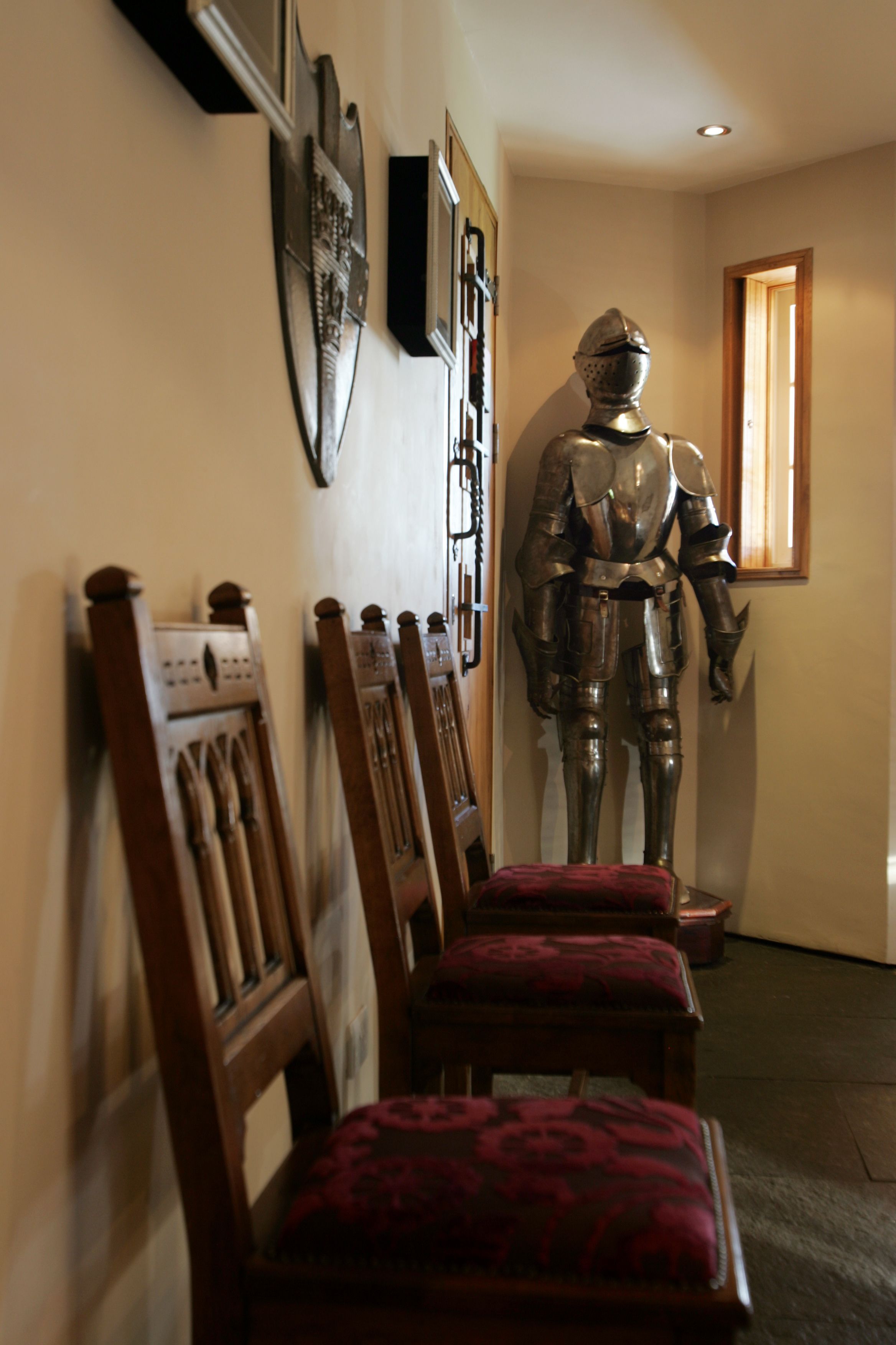 Corredor com cadeiras de madeira e uma estátua de armadura de cavaleiro.