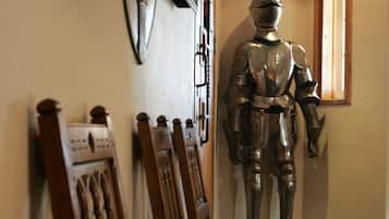 Corredor com cadeiras de madeira e uma estátua de armadura de cavaleiro.