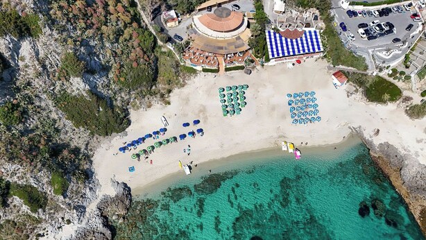 Vista aérea de una playa con aguas turquesas cristalinas, una orilla arenosa y varias sombrillas de playa.