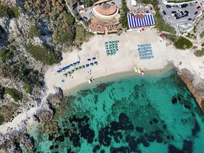 Vista aérea de una playa con aguas turquesas cristalinas, una orilla arenosa y varias sombrillas de playa.
