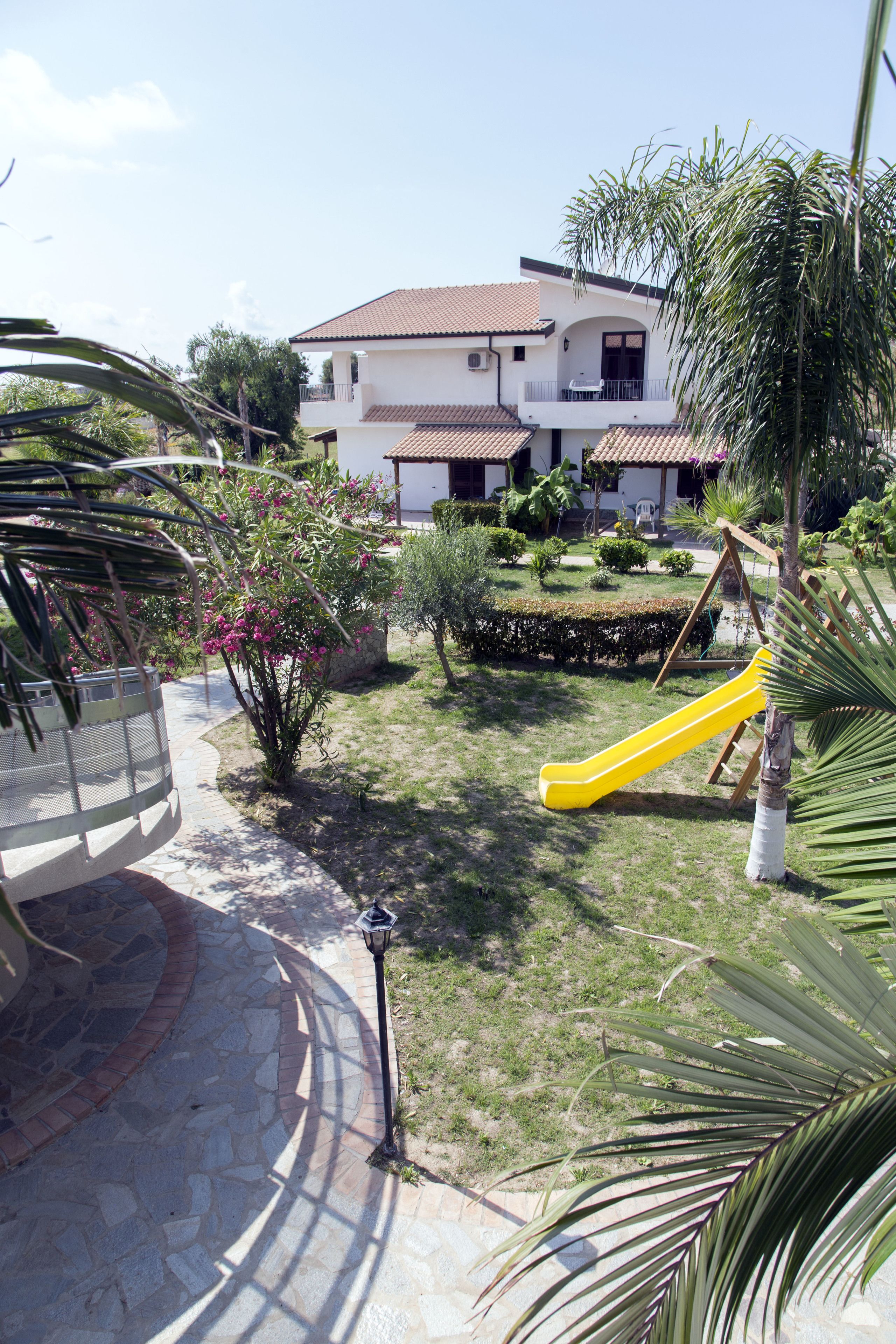 Un barrio residencial con una casa, un tobogán amarillo y un jardín con diversas plantas.