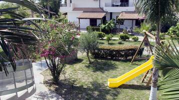 Un barrio residencial con una casa, un tobogán amarillo y un jardín con diversas plantas.