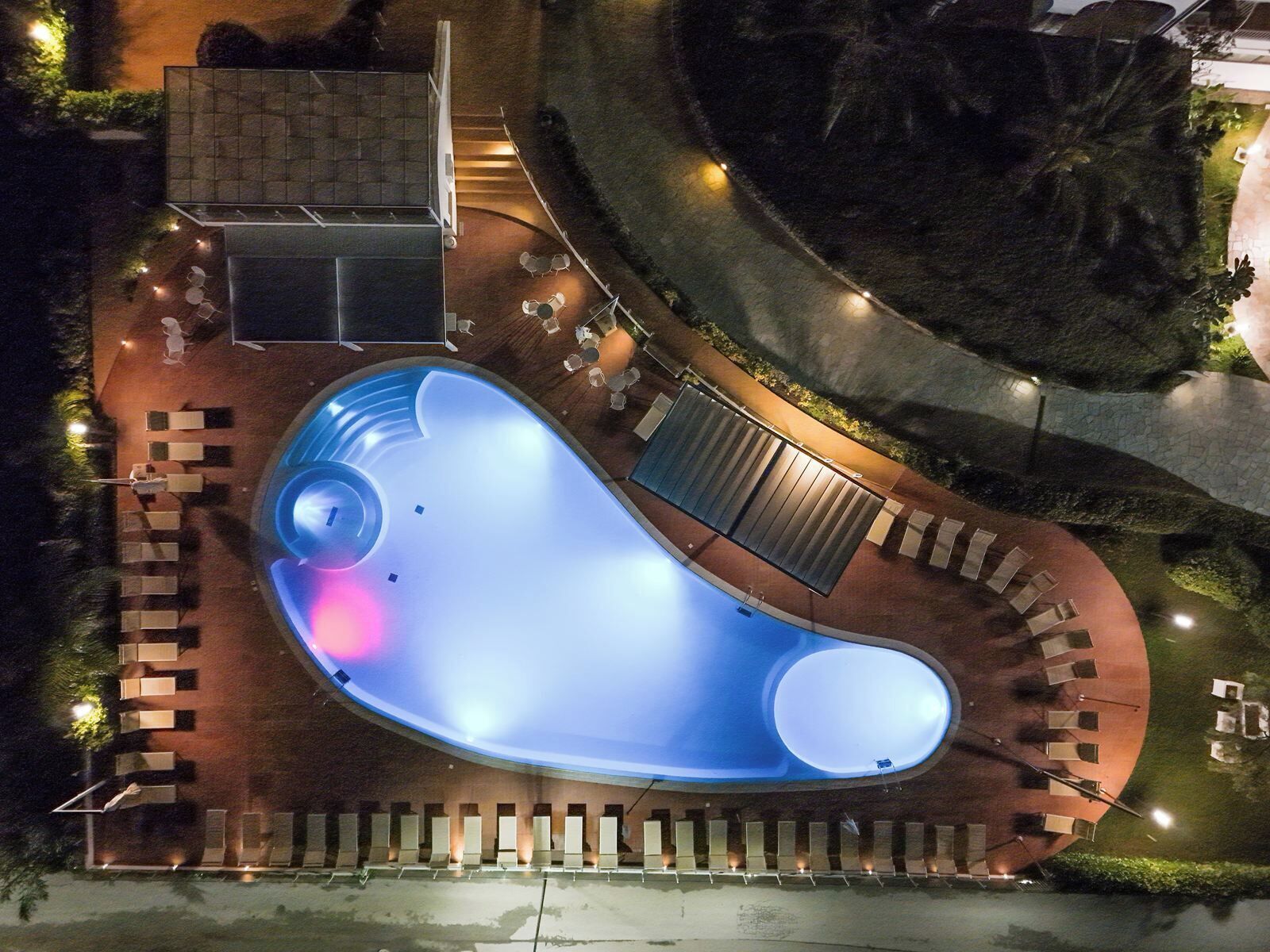 Vista aerea di una zona piscina con vasca a sfioro, circondata da lettini e una piccola terrazza.