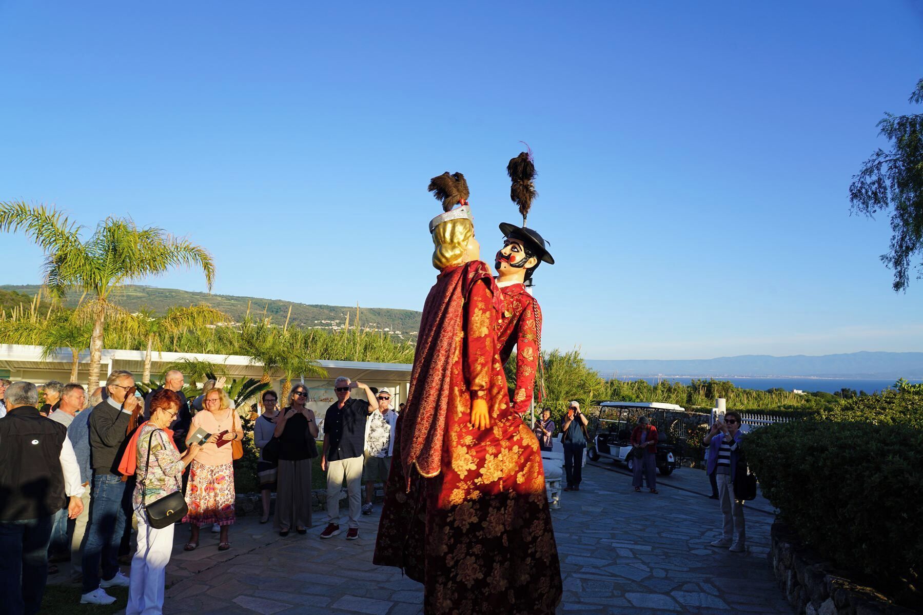 Un grupo de personas reunidas al aire libre, con una estatua de alguien vestido con traje tradicional y sombrero emplumado en primer plano.