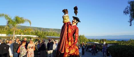 Un grupo de personas reunidas al aire libre, con una estatua de alguien vestido con traje tradicional y sombrero emplumado en primer plano.