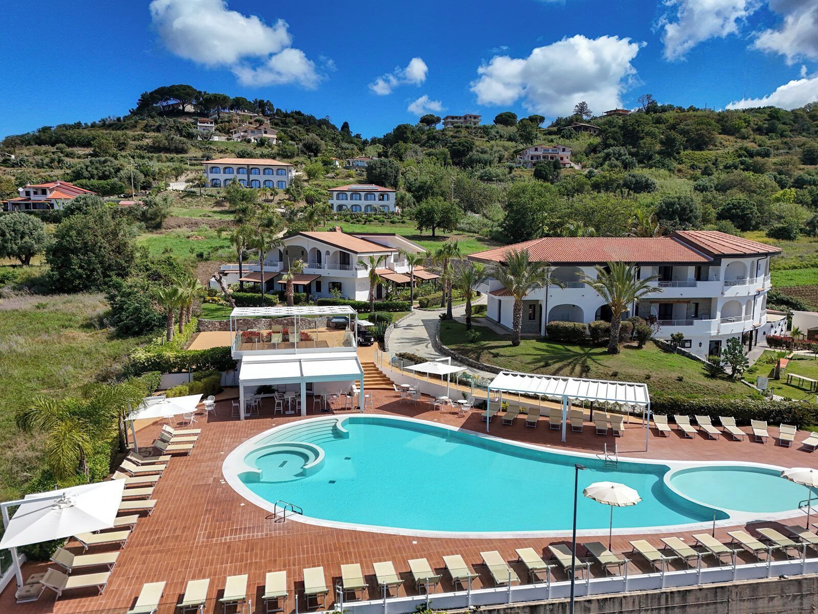 A resort with a large swimming pool, multiple villas, and a hillside backdrop.