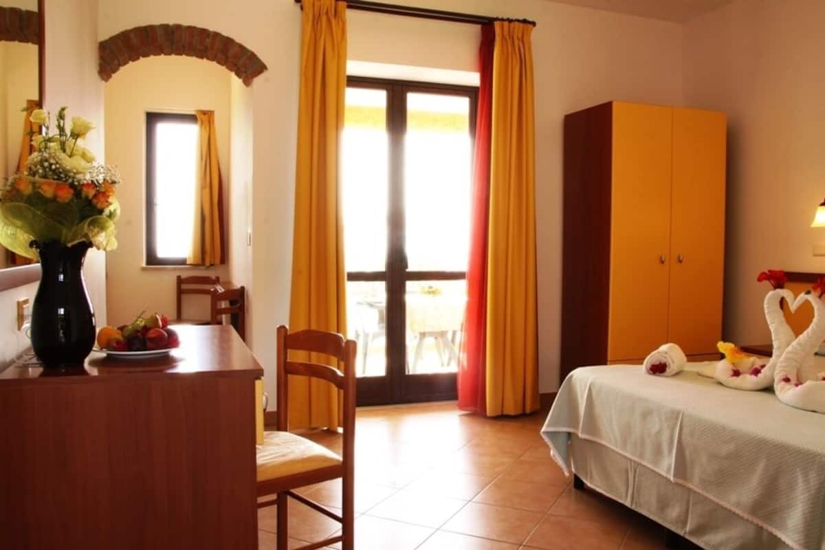 Ett hotellrum med en säng, ett skrivbord i trä med en vas med blommor, en stol och en garderob.