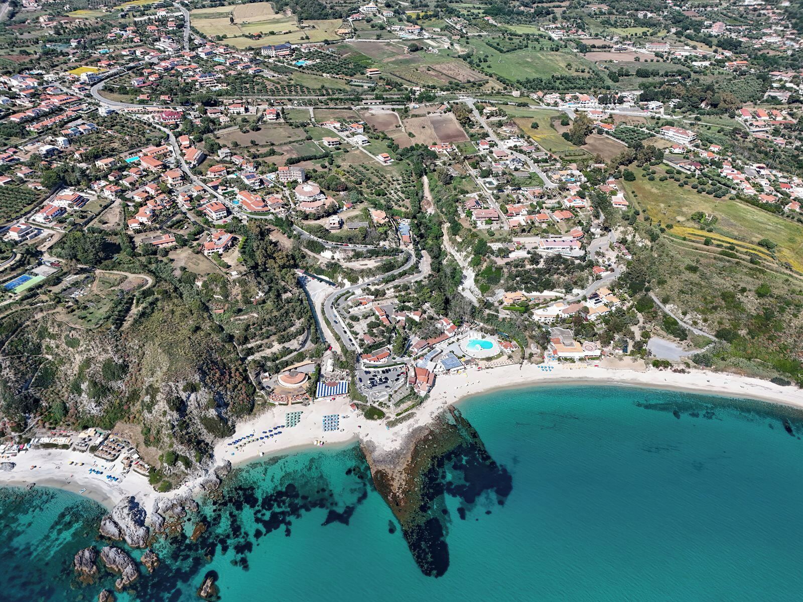 Eine Luftaufnahme einer Küstenstadt mit Strand, Wohngebieten und einem großen Gebäude mit Pool.