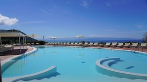 Piscina con tumbonas y sombrillas, rodeada de un cielo despejado y montañas al fondo.