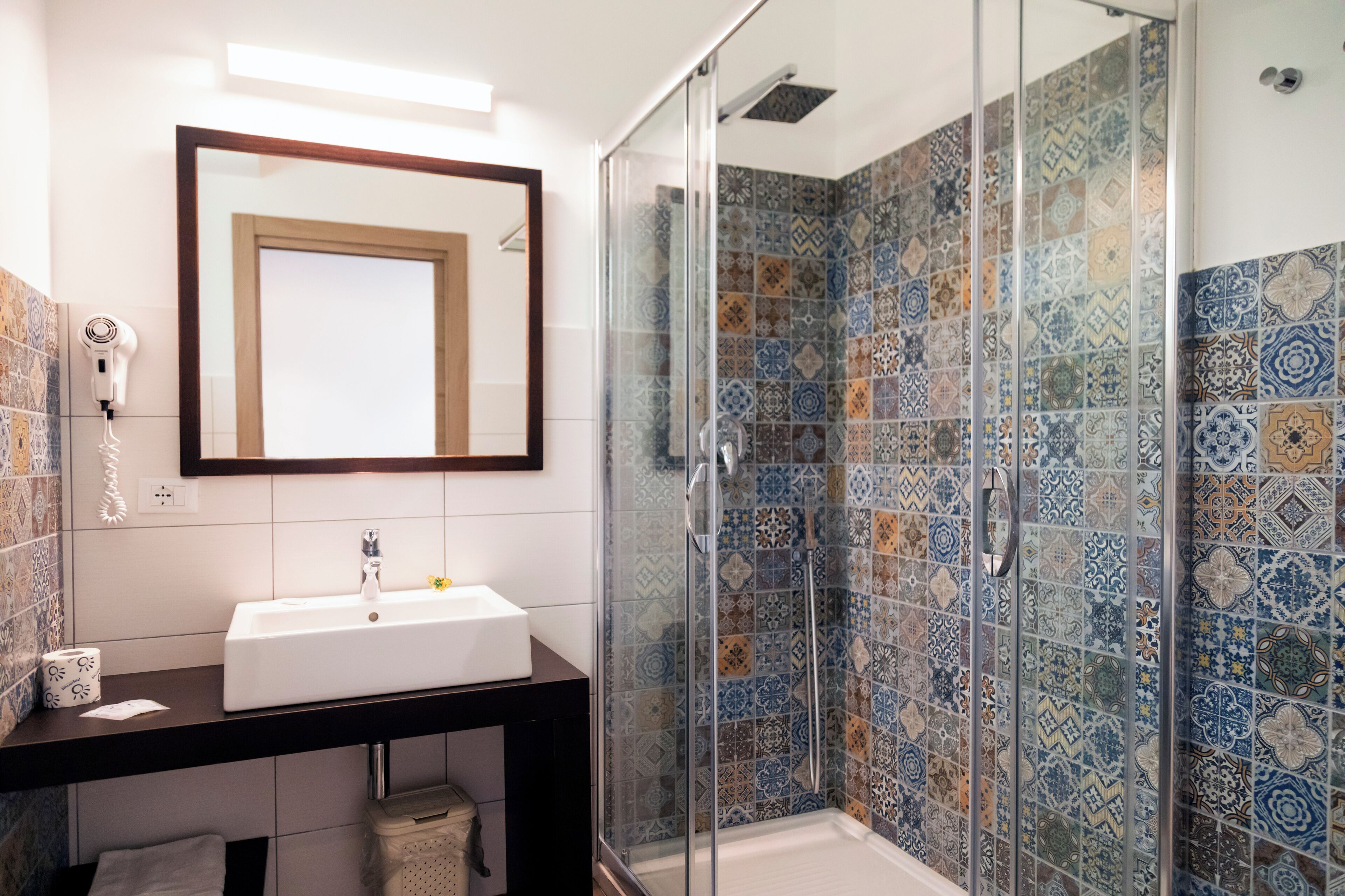 Une salle de bain avec un lavabo blanc, un miroir et une douche aux carreaux décorés.