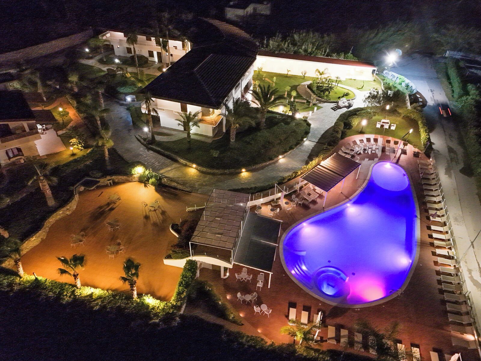 An aerial view of a resort with a swimming pool, lounge areas, and a building with a sloped roof.
