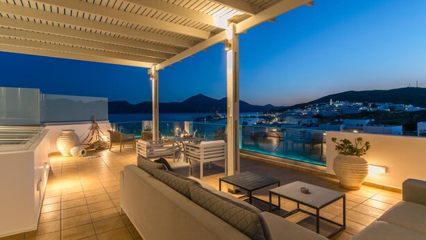 Une terrasse extérieure avec une piscine, des sièges et une vue sur une ville côtière au crépuscule.