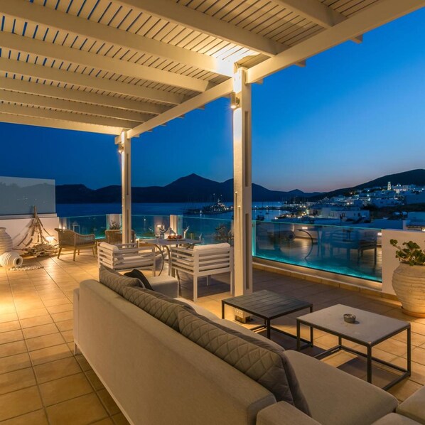 An outdoor terrace with a pool, seating area, and a view of a coastal town at dusk.