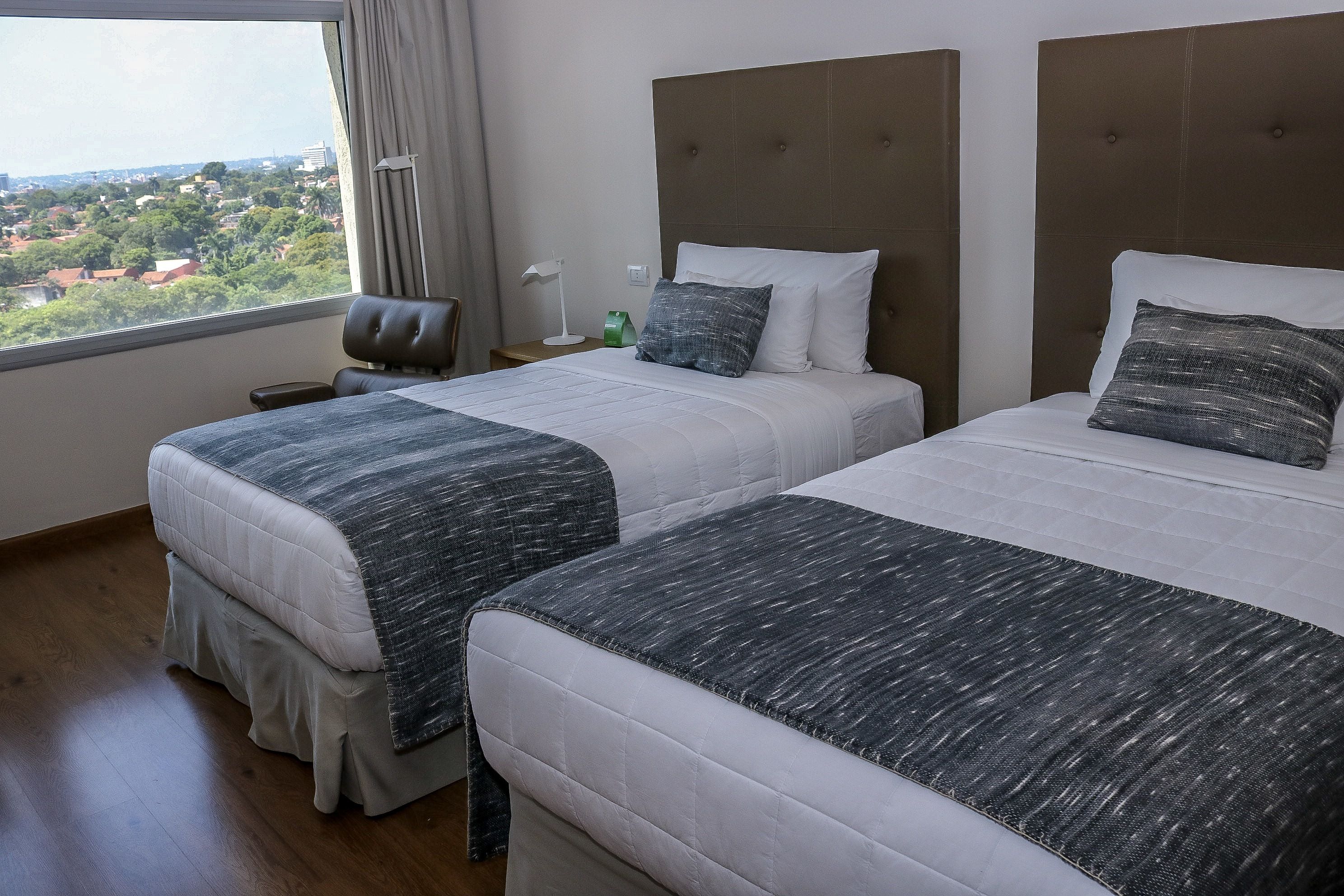 Habitación de hotel con dos camas, vista a un paisaje urbano y una ventana con cortinas.