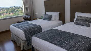 Habitación de hotel con dos camas, vista a un paisaje urbano y una ventana con cortinas.