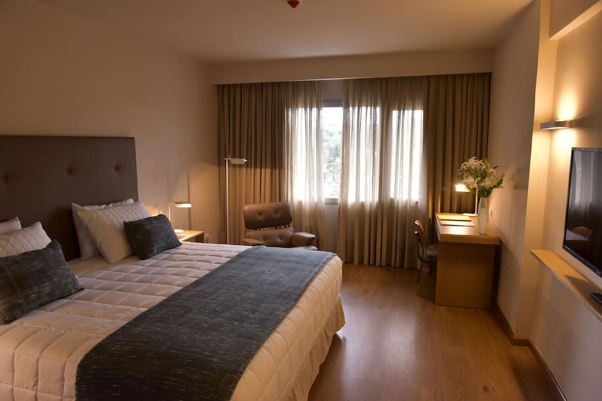 A hotel room with a bed, a desk, a chair, a TV, and a window with curtains.