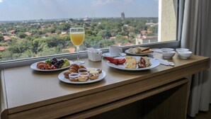 A breakfast table with plates of food, a glass of juice, and a view of a cityscape through a window. - Dazzler by Wyndham Asuncion (Asunción)