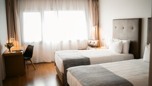 A hotel room with two beds, a desk, a chair, a lamp, and a window with curtains. - Dazzler by Wyndham Asuncion (Asunción)