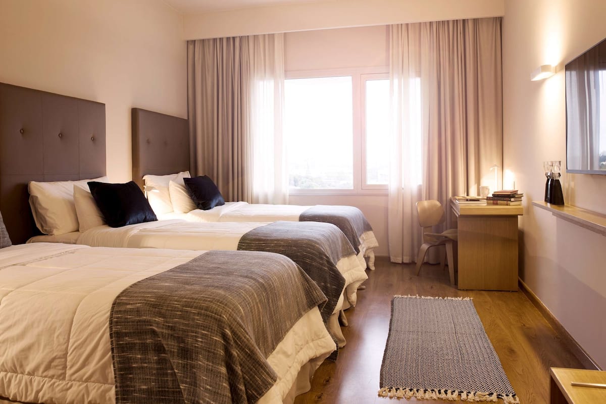 A hotel room with two beds, a desk, a chair, and a large window with curtains.