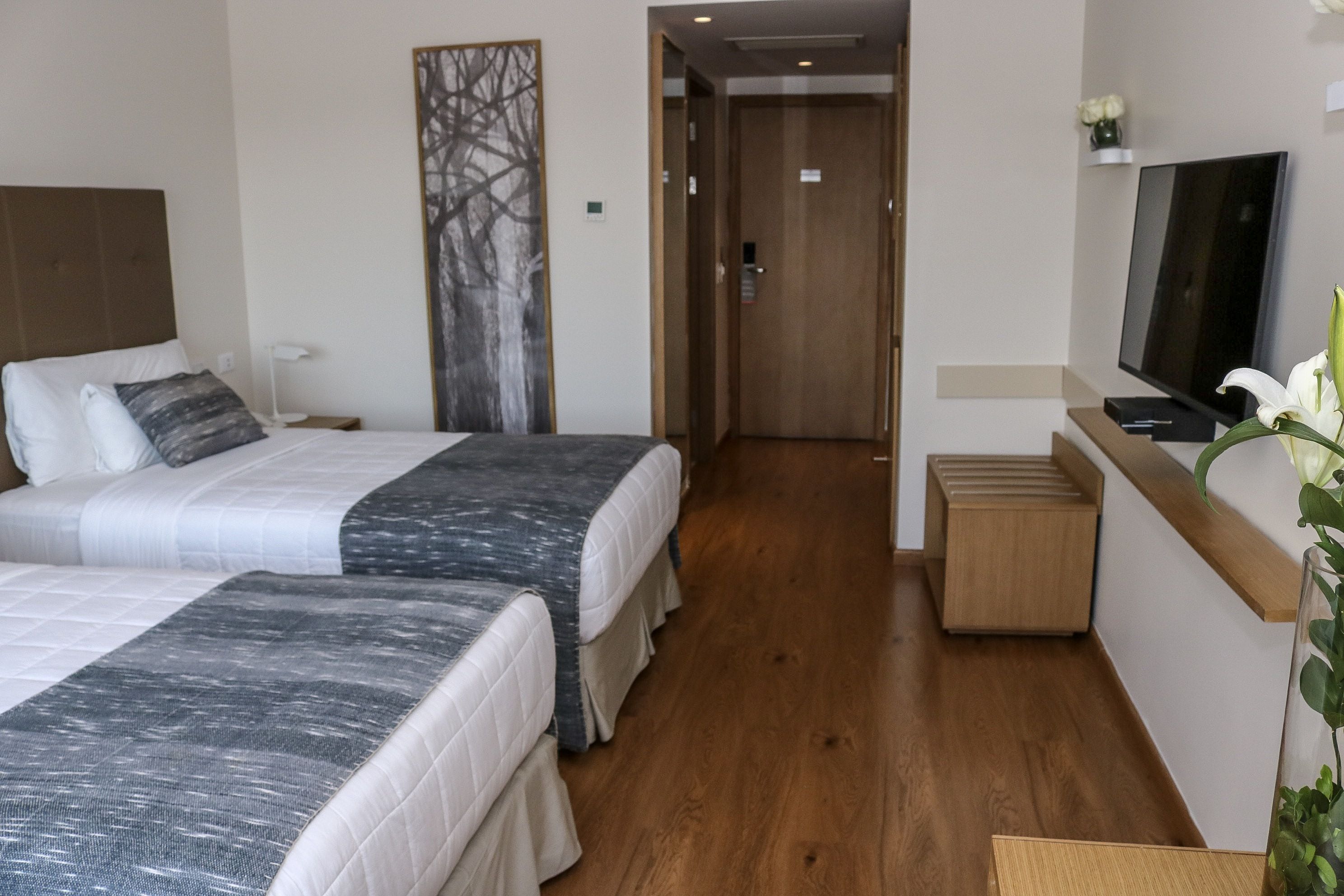 Ein Hotelzimmer mit zwei Betten, einem Fernseher, einem kleinen Holzhochentisch und einem Flur, der zu einem Aufzug führt.