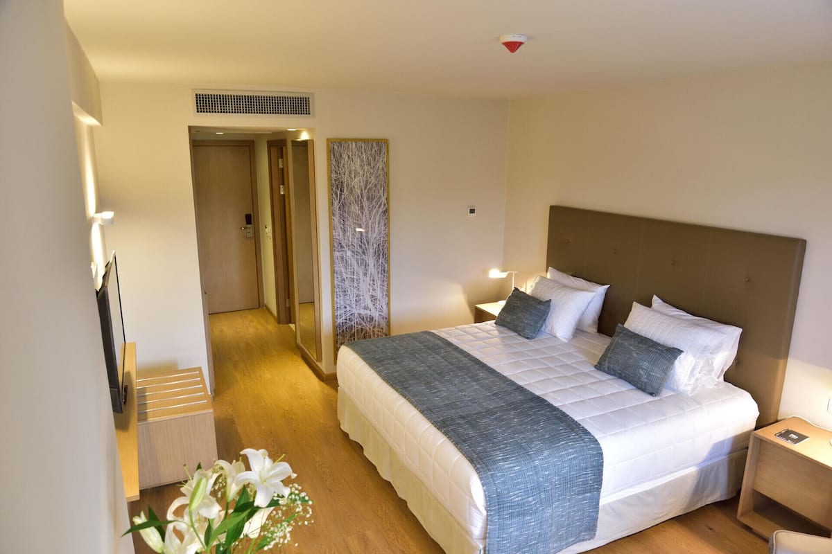 A hotel room with a large bed, bedside tables, a mirror, and a wall-mounted light fixture.