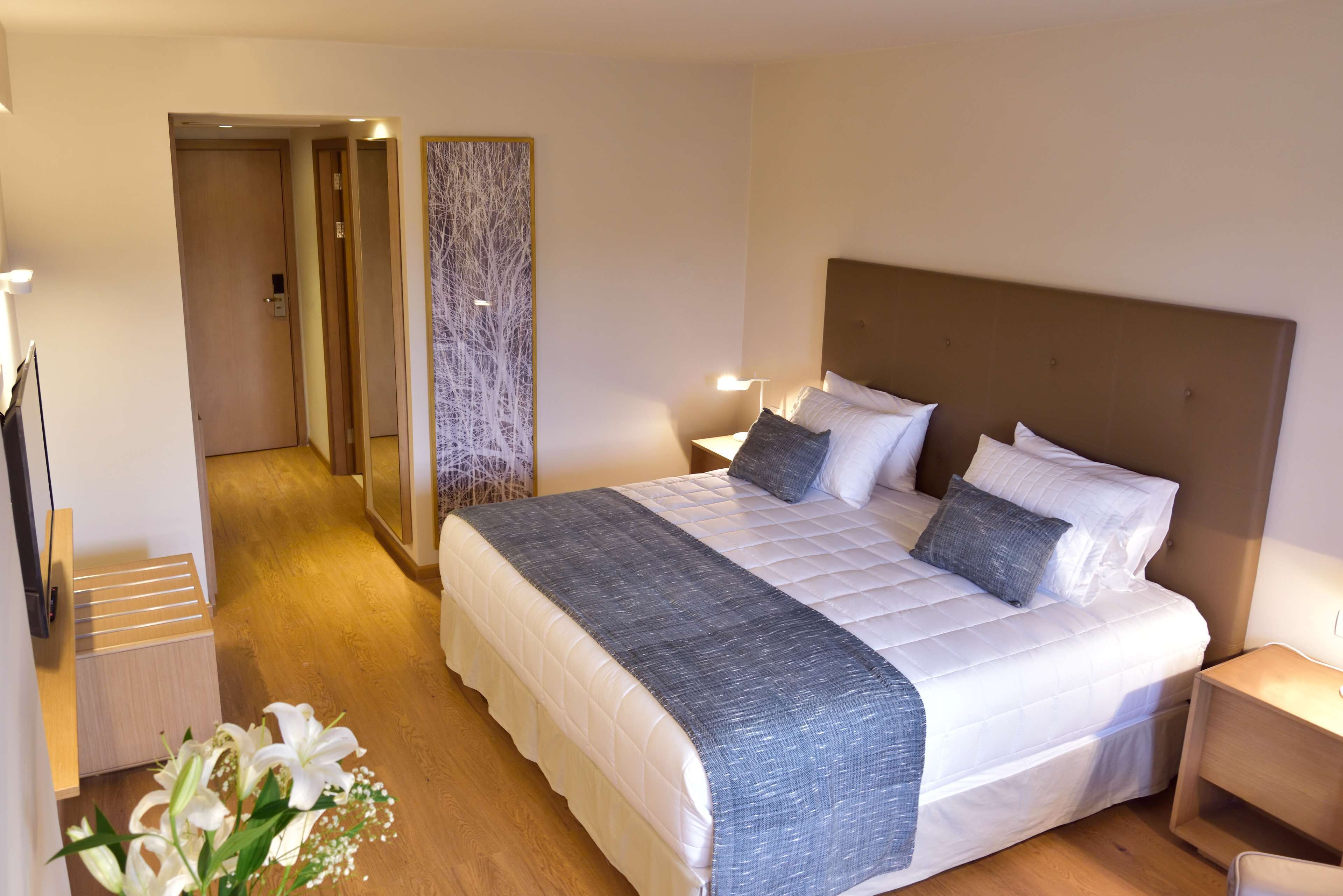 A hotel room with a large bed, bedside tables, a mirror, and a wooden floor.