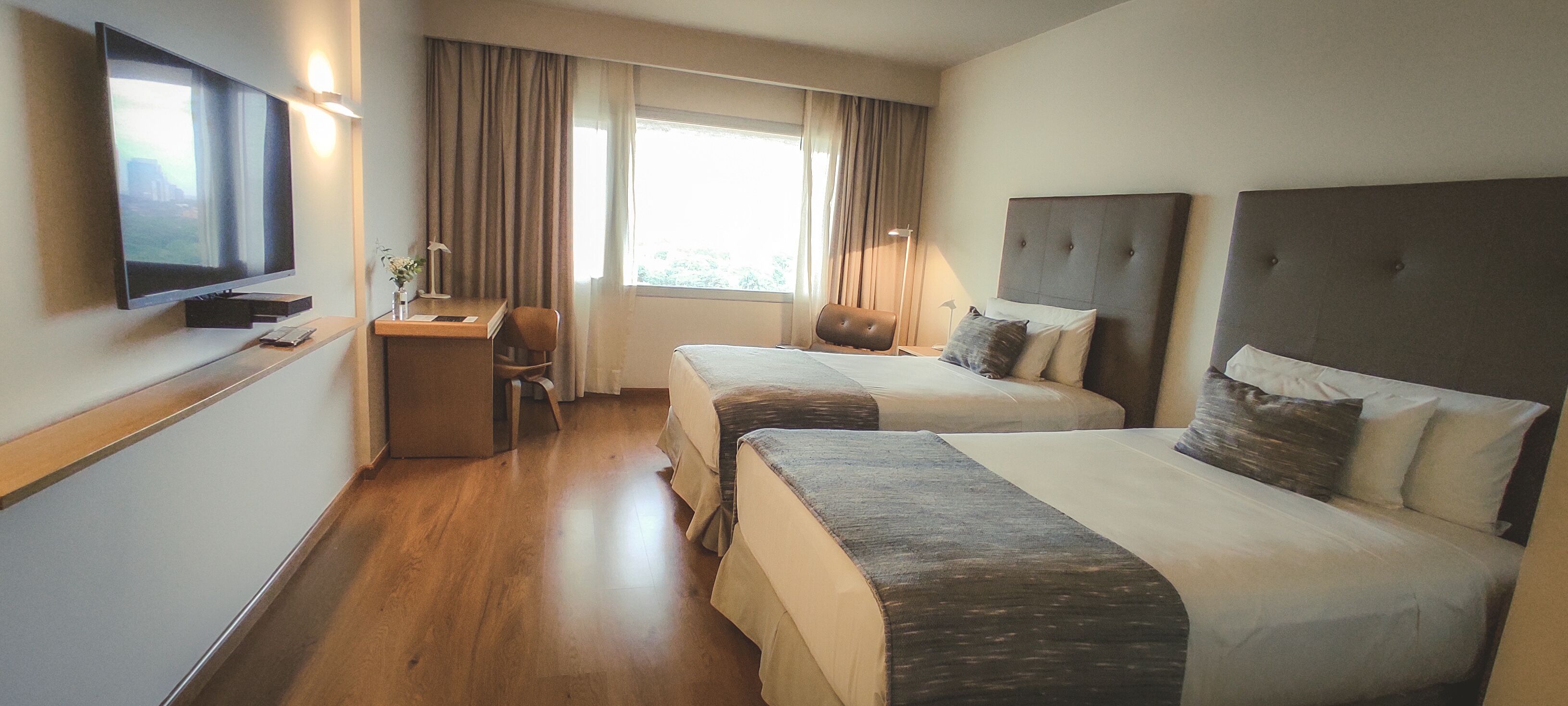 A hotel room with two beds, a desk, a chair, a TV, and a window with curtains.