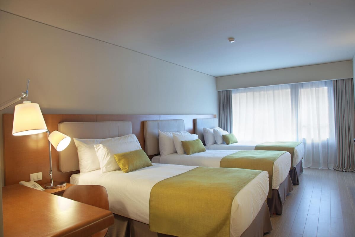 A hotel room with two beds, a desk, a lamp, and a phone.