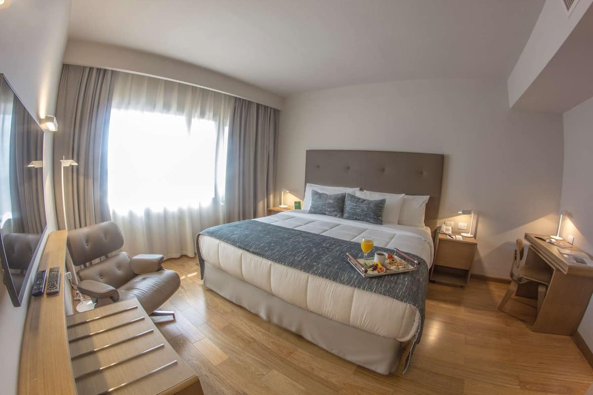 A modern hotel room with a large bed, a desk, a chair, and a TV.