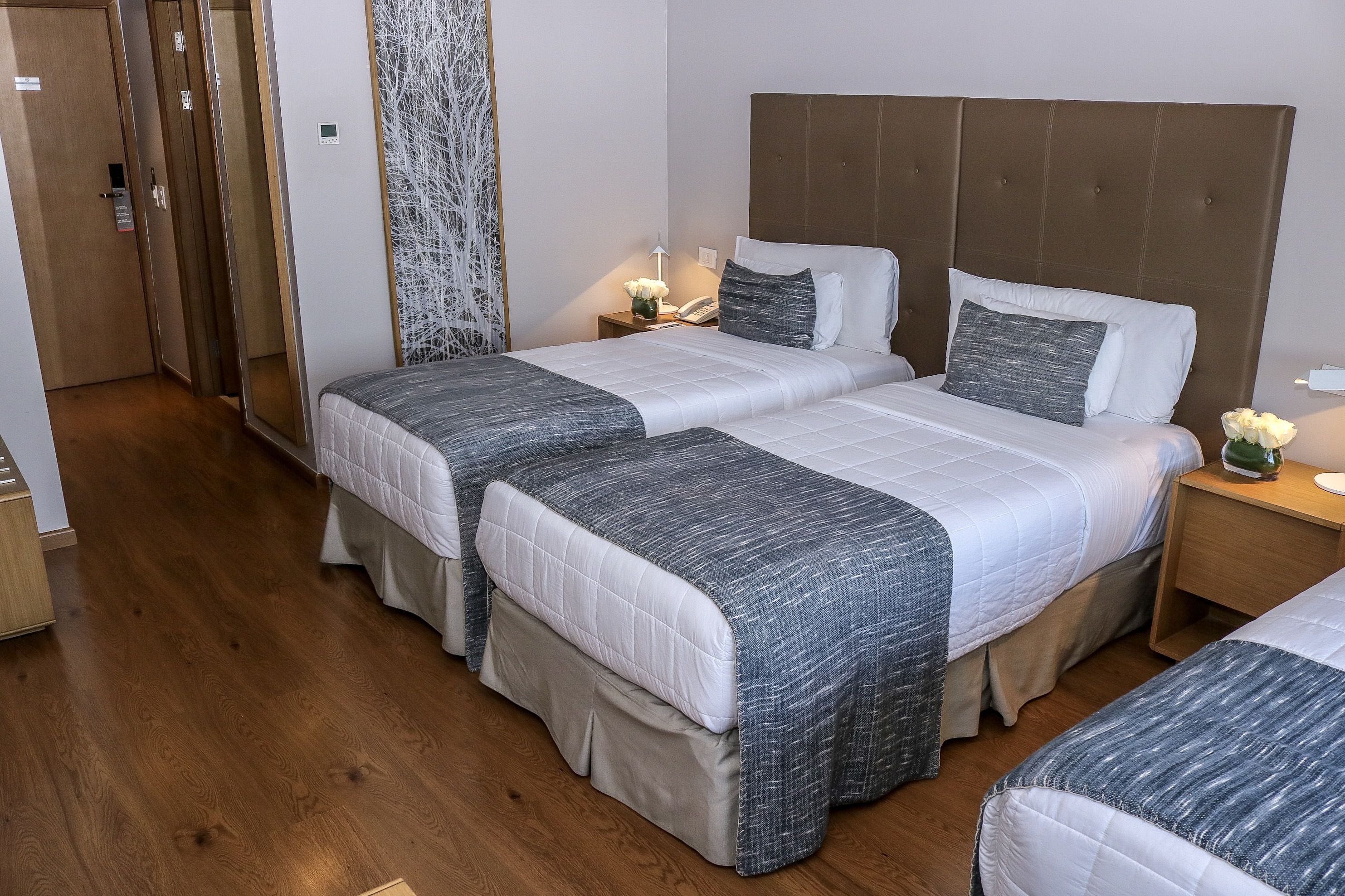 Une chambre d’hôtel avec deux lits, un plancher en bois, un miroir, une table de chevet avec une lampe et un téléphone fixé au mur.