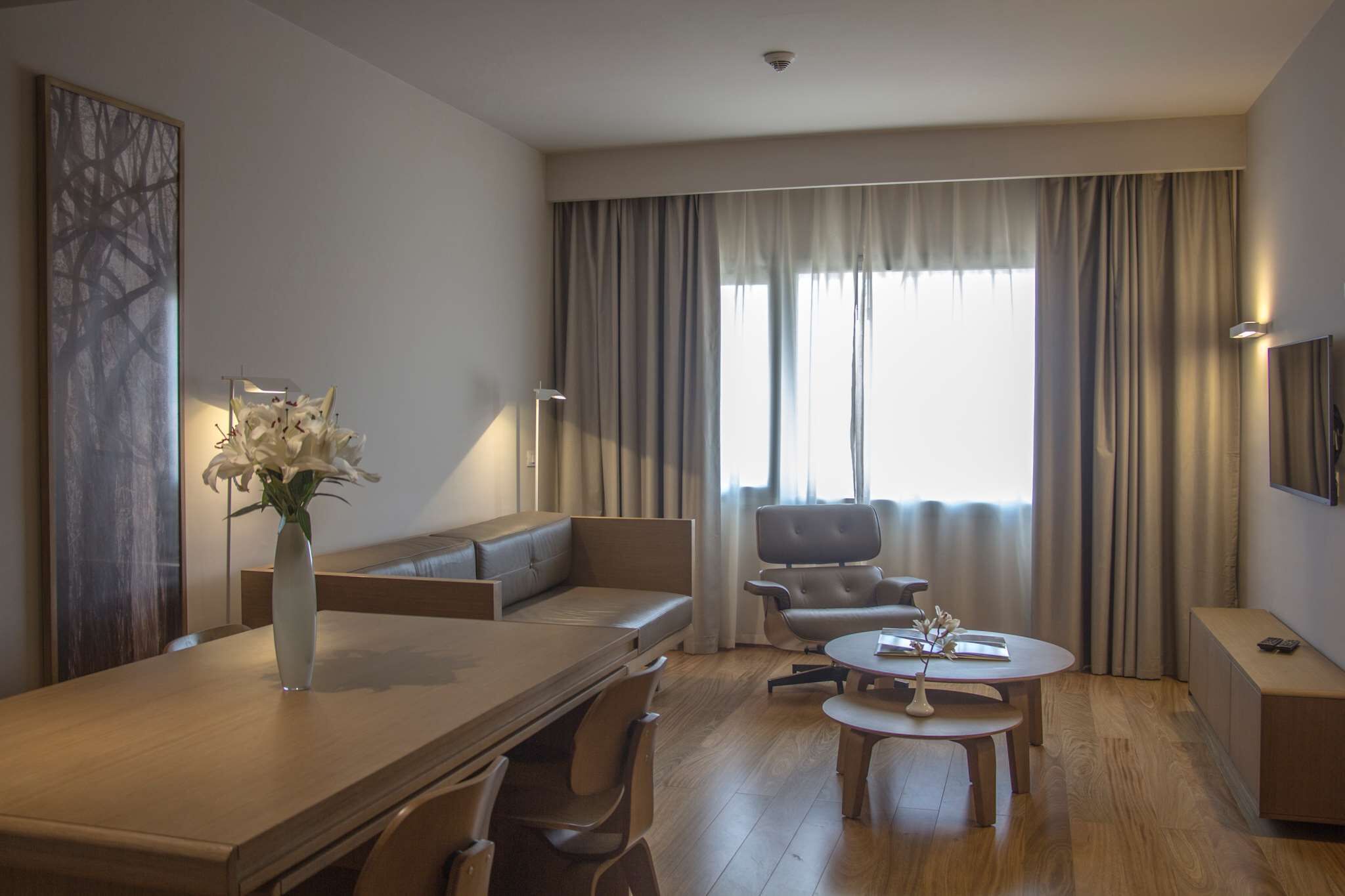 Una habitación de hotel moderna con zona de comedor, sofá, sillón y televisor en la pared.