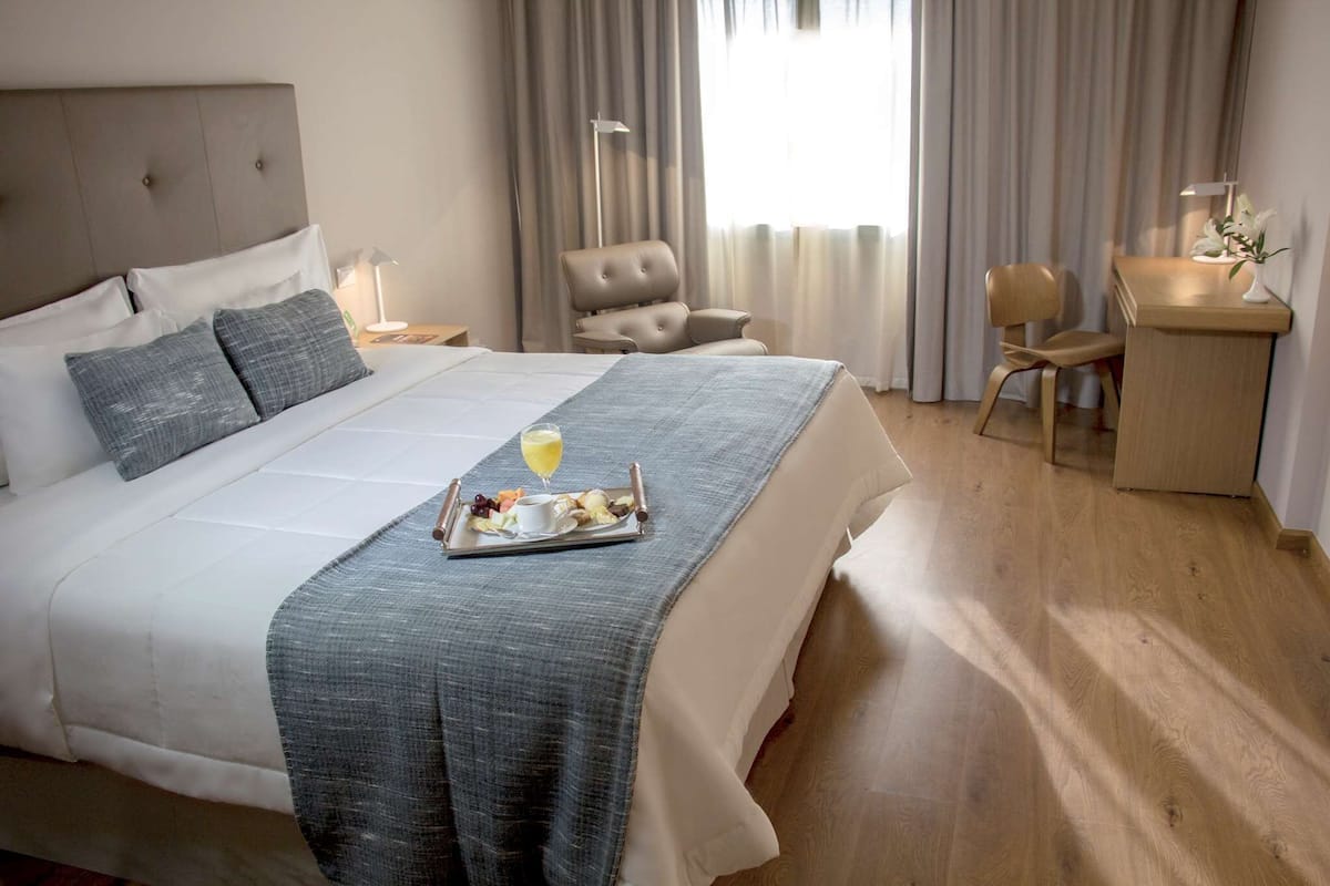 A hotel room with a large bed, a desk, a chair, and a window with curtains.