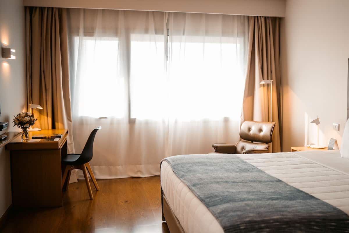 A hotel room with a bed, a desk, a chair, and a window with curtains.