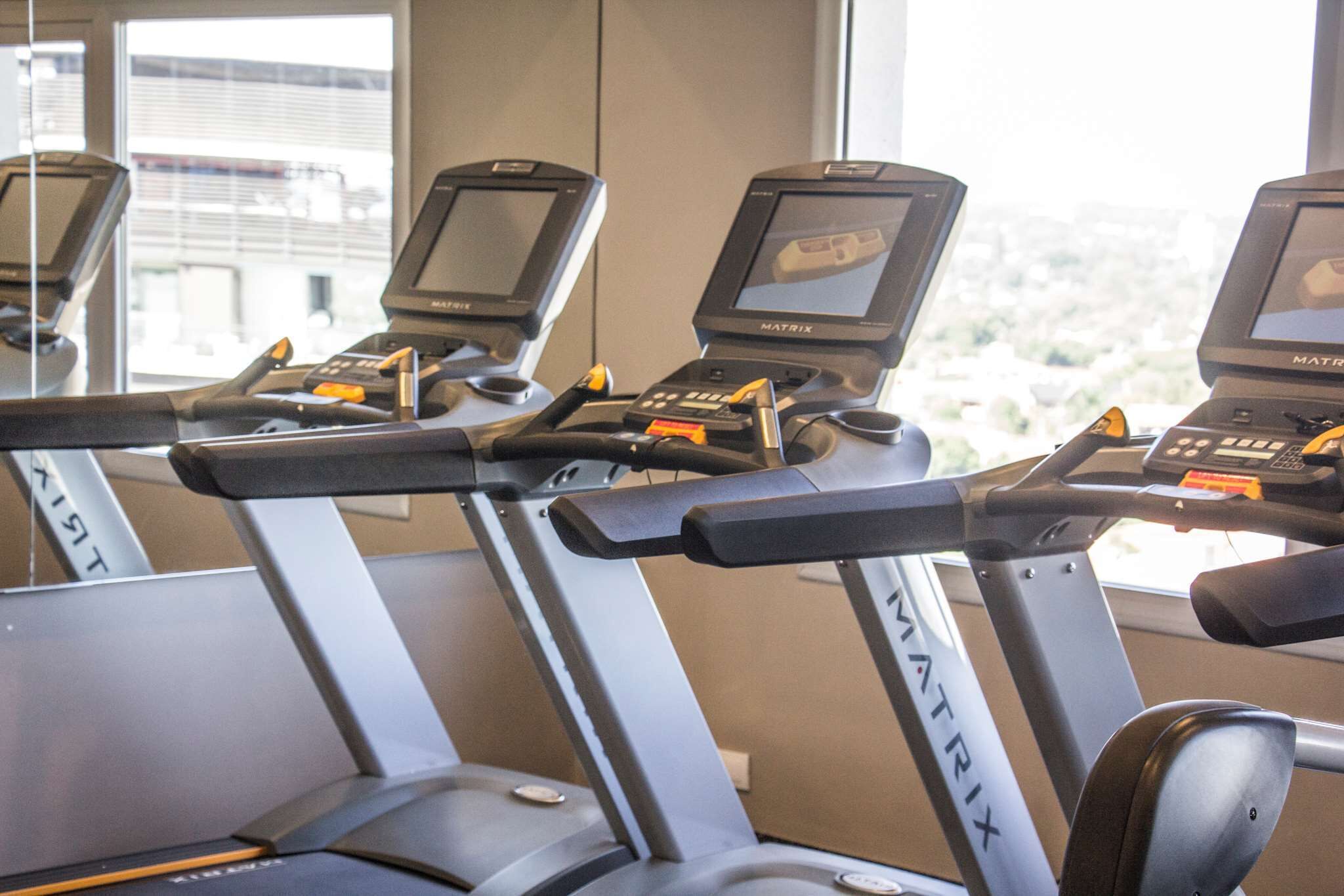 A row of Matrix brand stationary bikes in a gym with large windows.