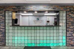 Un espace d’accueil avec un mur en pierre, une cloison en verre et une enseigne indiquant « Quality Inn & Suites by CHOICE Hotels ».
